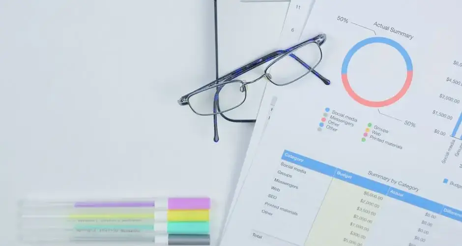 A modern workspace featuring budget graph, laptop, glasses, and stationery for creative business planning.