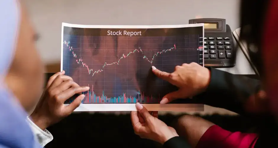 Two professionals discuss a stock report chart in a business meeting, analyzing data trends.