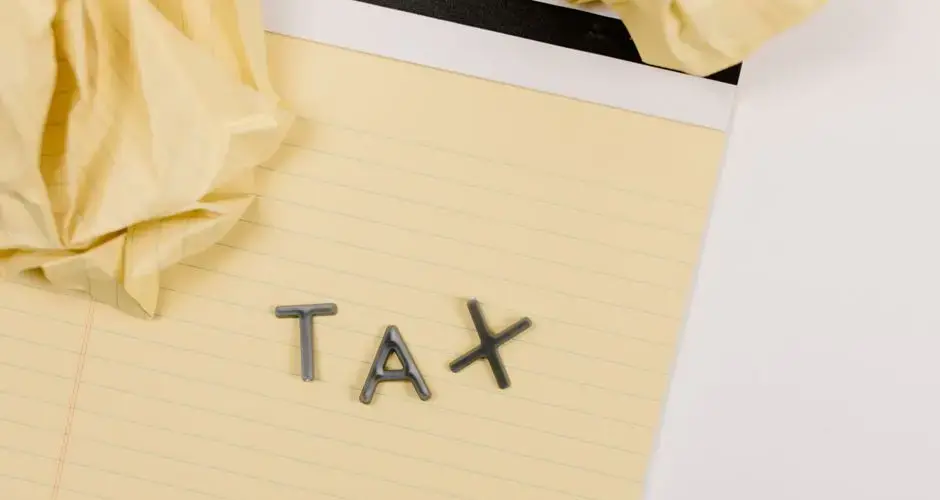 Close-up of a yellow lined paper with metal letters spelling 'tax', surrounded by crumpled paper.