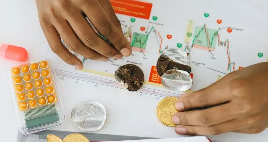 Analyzing financial charts with a calculator and chocolate coins.