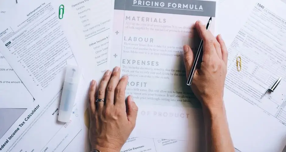 Hands organizing business documents and pricing formula papers on an office desk.