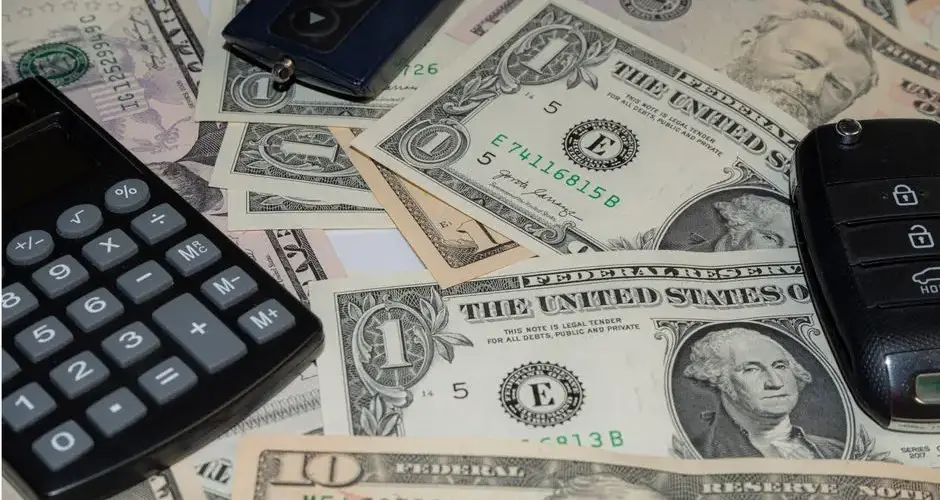 Close-up of various US banknotes, calculator, and car key illustrating finance concept.