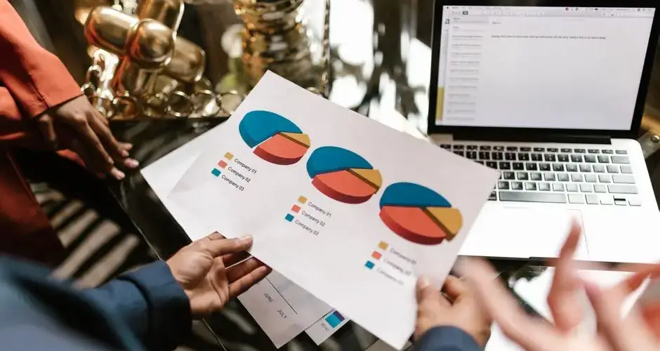 Professional hands holding pie chart data near laptop in modern office setting.