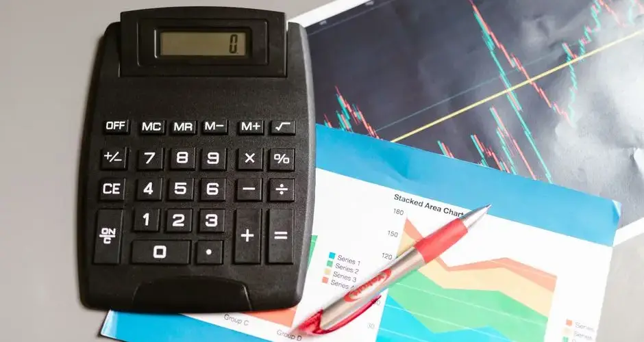 Calculator and pen on a desk with financial charts, showcasing analysis and business planning.
