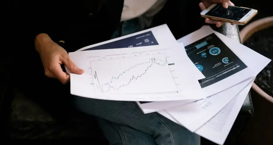A person reviews stock market graphs on paper and smartphone for business insights.