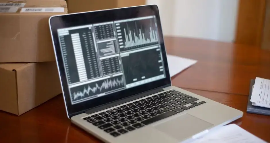 Laptop showing data graphs on wooden table with cardboard boxes, depicting a small business office setting.