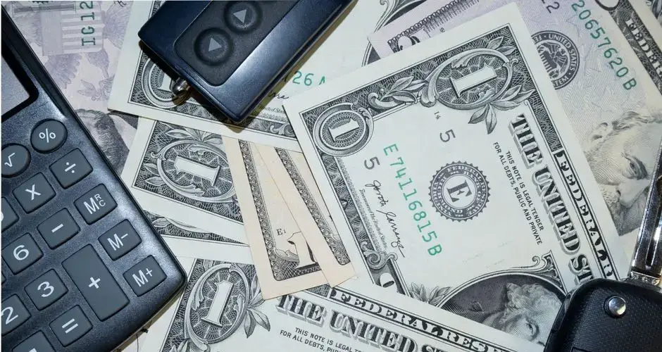 An arrangement of US dollar bills, car keys, and a calculator representing finance and investment concepts.