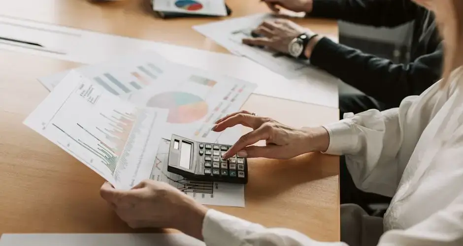 Hands performing financial calculations with charts and a calculator at a meeting table.