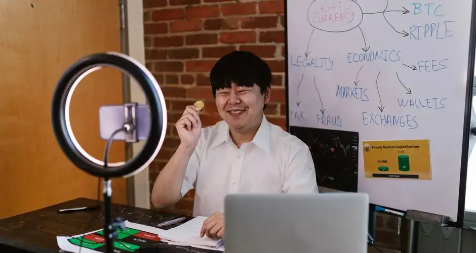 Man discussing cryptocurrency concepts online with a laptop, ring light, and whiteboard.