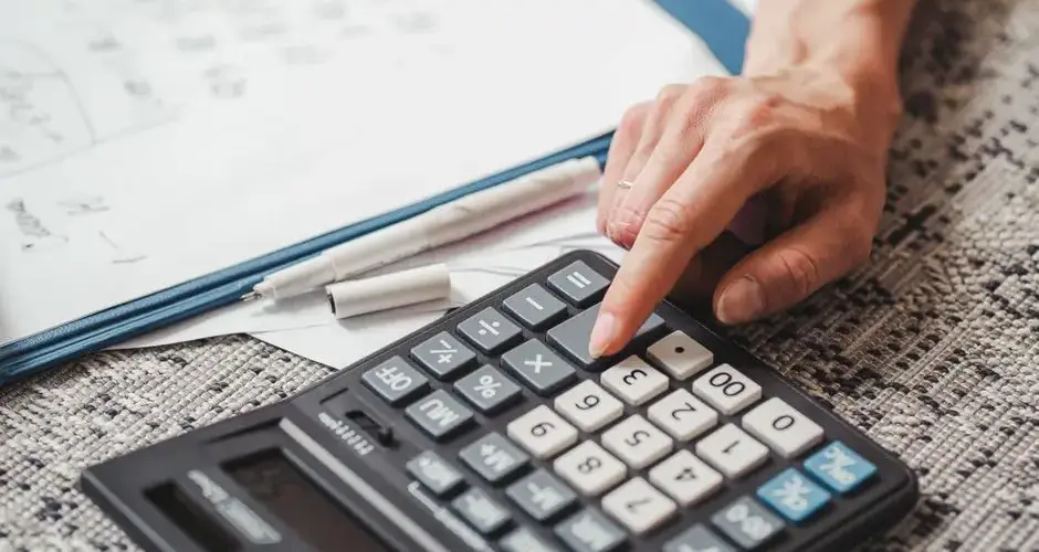 A hand using a calculator on top of documents, indicating financial calculation or analysis.