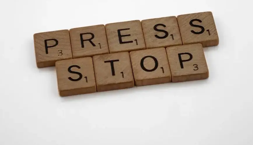 Wooden Scrabble tiles forming the words 'Press Stop' on a white surface.