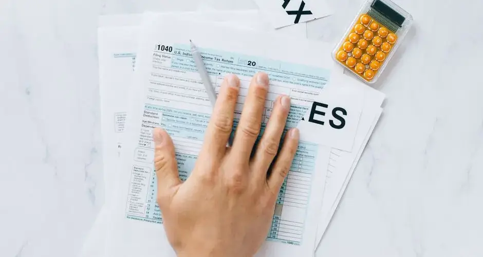 Close-up of a hand on tax form 1040 with a calculator on a desk.