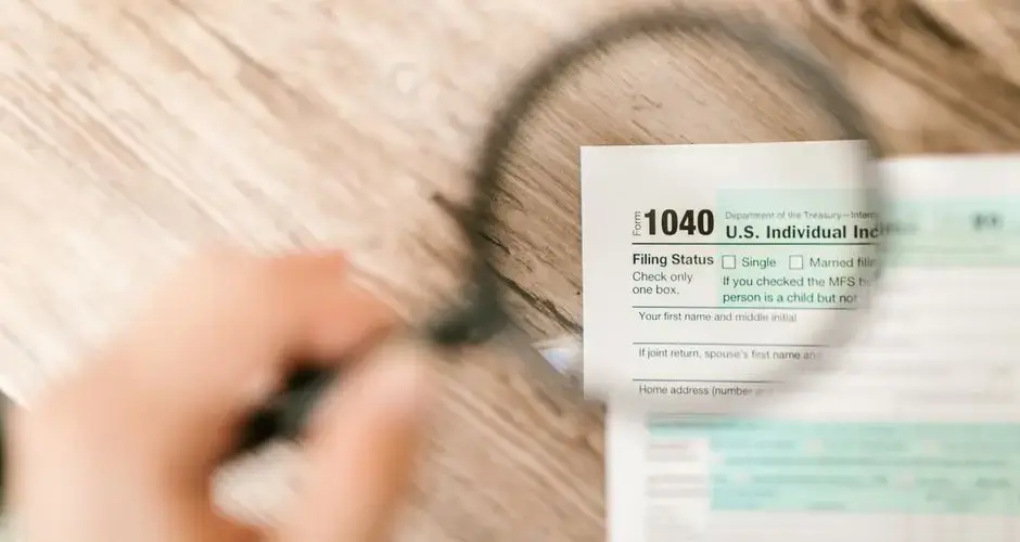 Close-up image of IRS Form 1040 under a magnifying glass on a wooden surface.