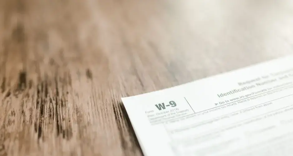 A close-up of a W-9 tax form placed on a wooden desk, emphasizing paperwork and finance.