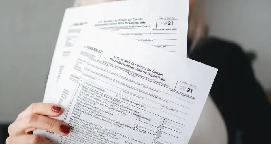A woman holds U.S. tax documents with a blurred background, implying focus on paperwork.