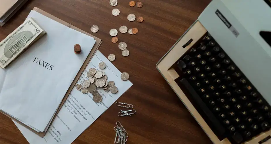 Overhead view of a vintage desk with typewriter, coins, and tax documents.