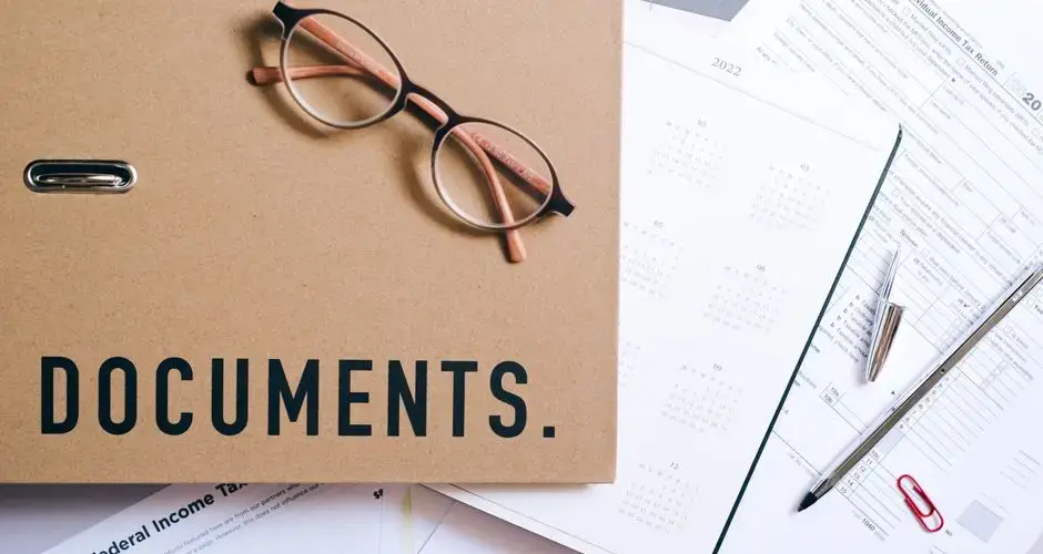 Flat lay of office supplies including documents, calendar, and eyeglasses on a desk.