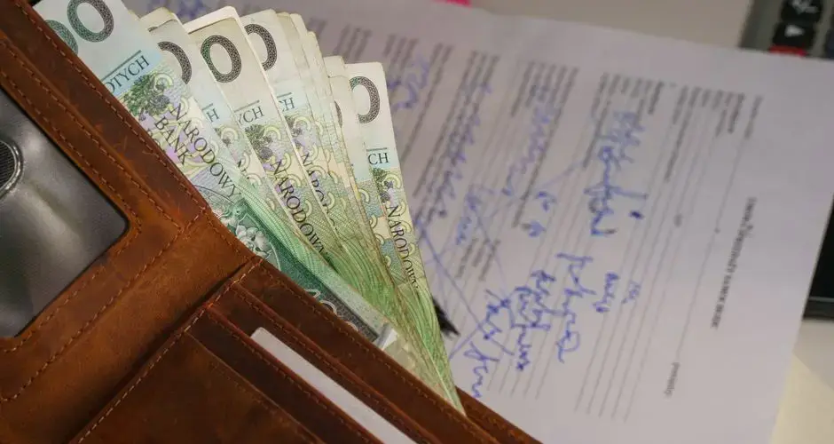 Close-up of a wallet containing Polish Zloty with a signed document in the background, representing financial transactions.