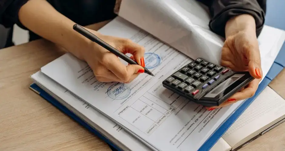 An accountant using a calculator and signing paperwork, showcasing financial analysis.