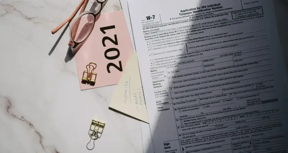 Flat lay of IRS tax documents with reading glasses and 2021 note on a marble surface.
