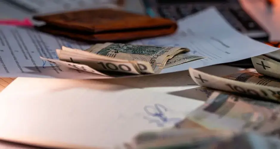 Zloty banknotes and financial paperwork scattered on a desk, representing budgeting and finance.