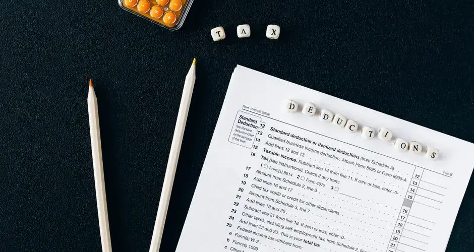 Flat lay of tax form, pencils, and calculator on black background, emphasizing tax deductions.