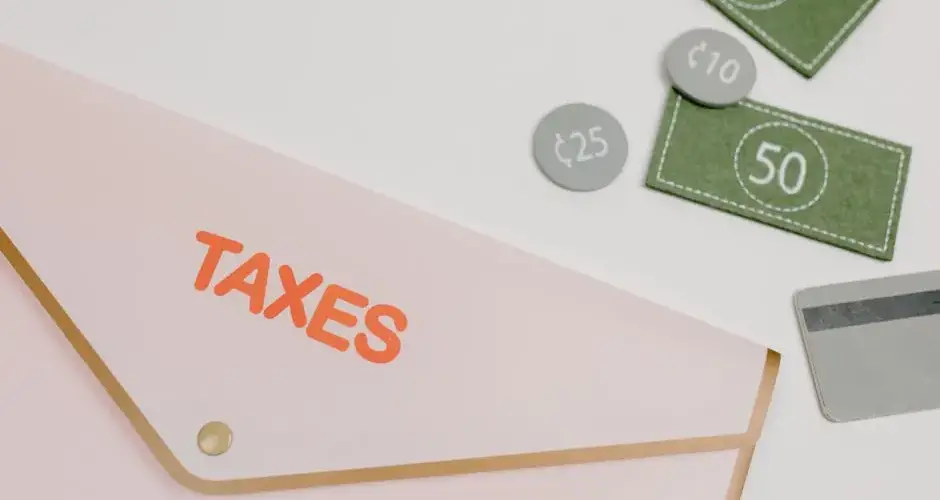 Pink envelope labeled 'TAXES' with play money and card on white background.