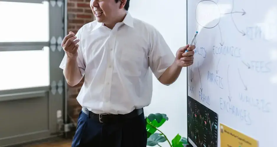 Asian man enthusiastically explaining financial concepts on a whiteboard in a modern office setting.