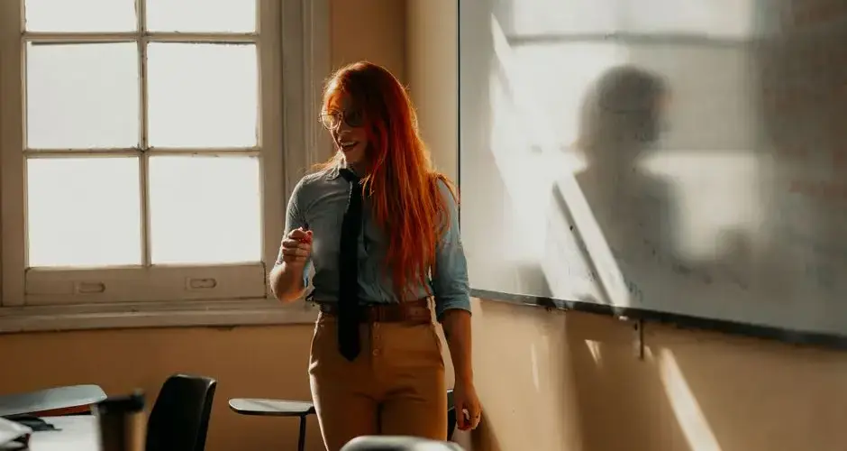 Smiling female teacher explains concepts on a whiteboard in a sunlit classroom in Buenos Aires.