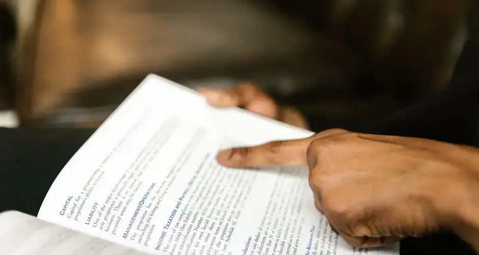 A person points to text in a book, highlighting finance content.