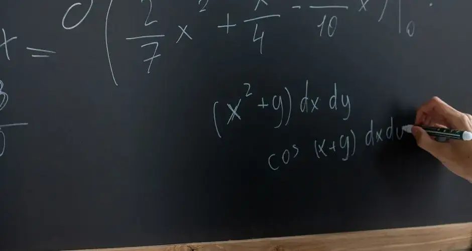Hand writing mathematical equations on a chalkboard in a classroom setting.