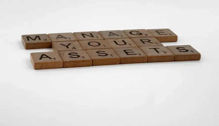 Wooden Scrabble tiles spelling 'Manage Your Assets' on a white background.