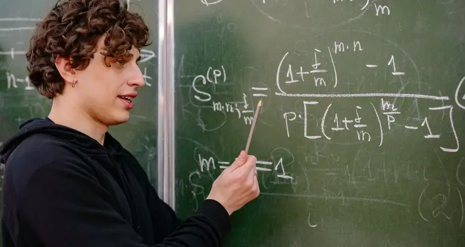 A young male educator explaining complex math equations at a university classroom blackboard.