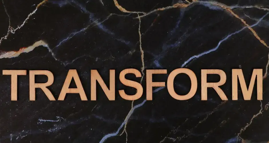 The word 'TRANSFORM' in wooden letters on a dark marble background, symbolizing change.