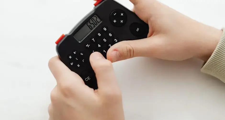 Close-up of hands using a portable black calculator with a digital display on a white background.