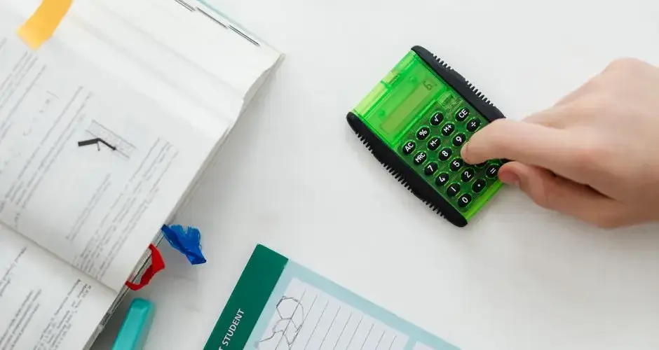 A student uses a green calculator to solve math equations from a textbook on a desk.