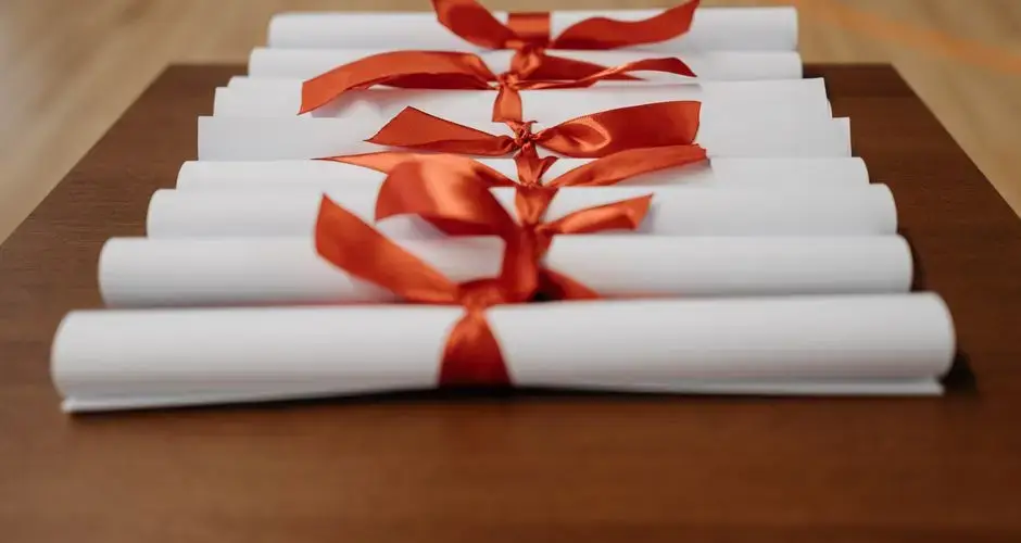 Close-up of rolled diplomas tied with red ribbons on a wooden desk, ready for presentation.