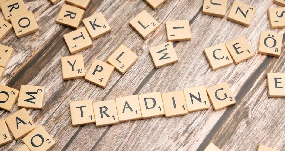 Wooden Scrabble tiles spelling 'TRADING' against a rustic wood background.