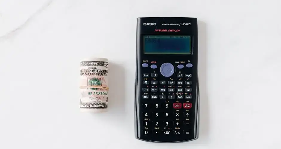 Top view of calculator with plastic multicolored buttons and display near roll of dollar banknotes tied with rubber band on white surface