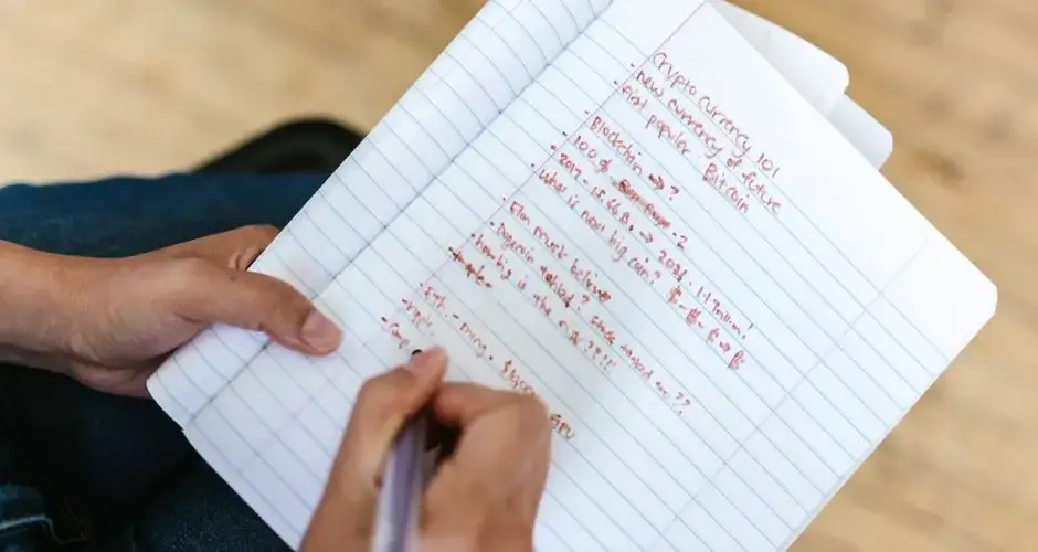 A person writing cryptocurrency notes in a notebook, highlighting Bitcoin and future predictions.