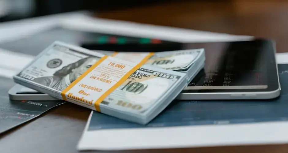 A stack of $100 bills placed on a tablet displaying financial graphs, representing modern finance.