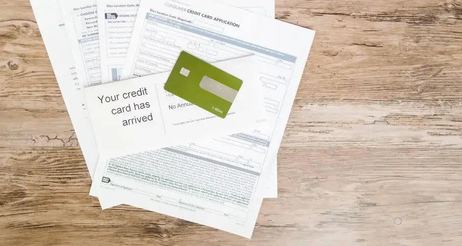 Top view of credit card and application documents on wooden surface.