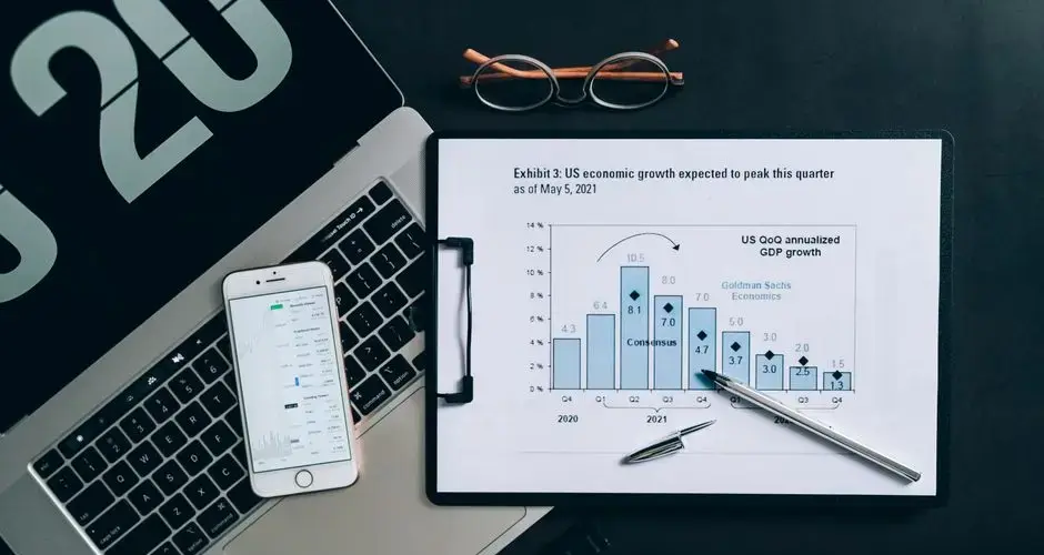 Top view of a financial data analysis setup with laptop, smartphone, and graph on clipboard.