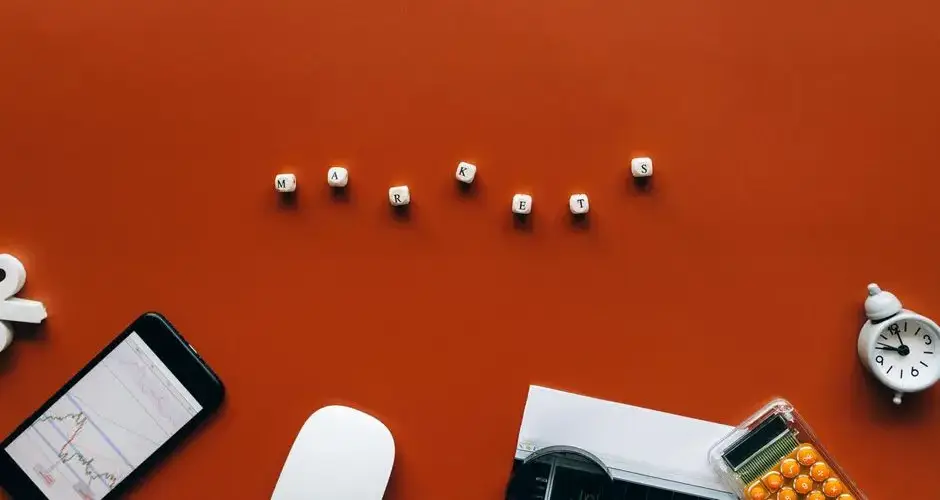 Creative still life with financial tools and the word 'MARKETS' on an orange background.