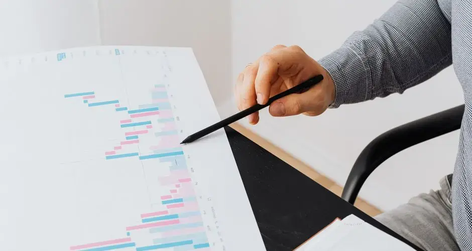 Close-up of a person analyzing a colorful graph chart with a pen in a modern office setting.