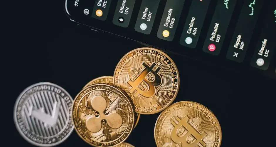 Close-up view of various cryptocurrency coins with a digital market display in the background.