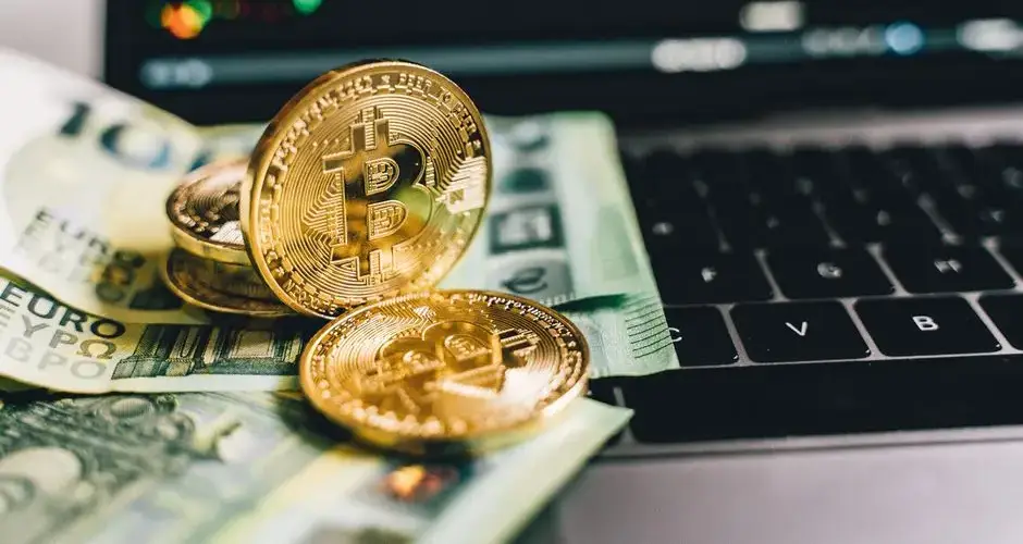 Bitcoin coins and Euro banknotes on a laptop with stock graph in background.