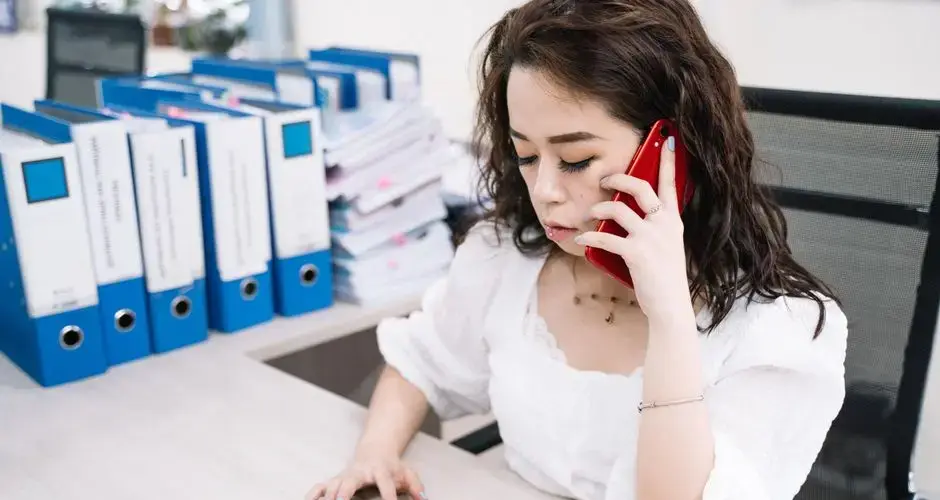 Businesswoman multitasking with calculator and cell phone at office desk.