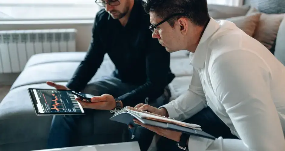 Two businessmen analyzing financial data on a tablet in a modern office setting.