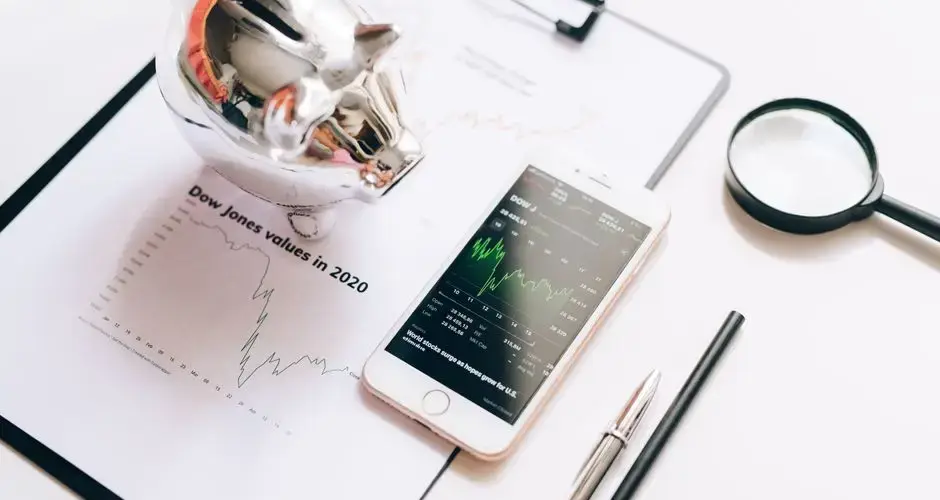 Flat lay of financial tools: chart, smartphone, magnifying glass, and piggy bank.